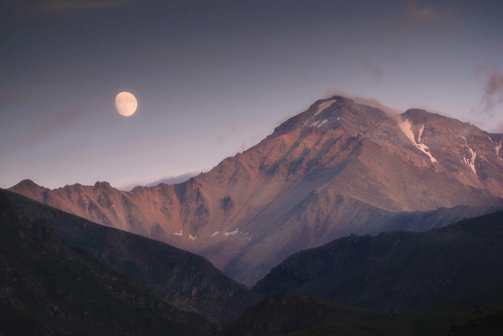 A full moon rising over mountains at dusk