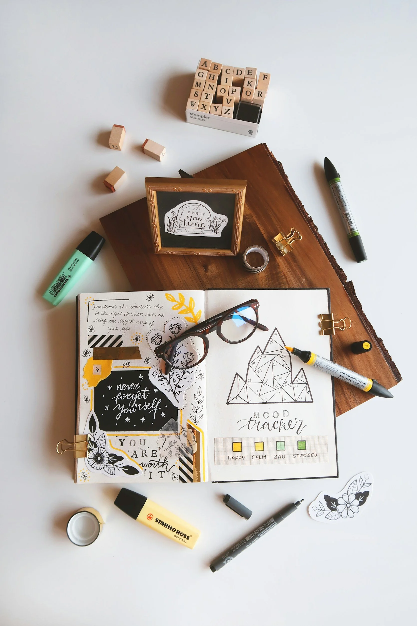 An open journal with a hand-drawn mood tracker, glasses, and pens