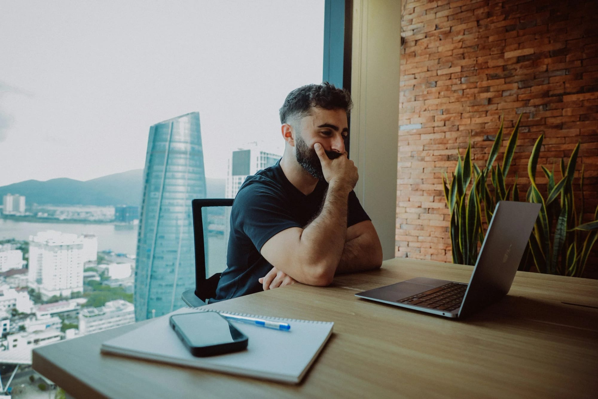 A young professional pausing at his desk, looking out over a city skyline